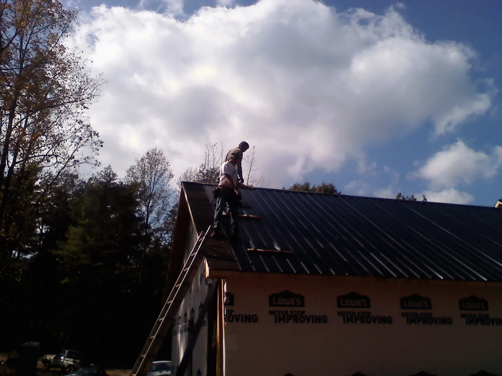 Roofer fastening dark metal panels high against a cloudy sky, from a Roof Inspection job in New Hampton