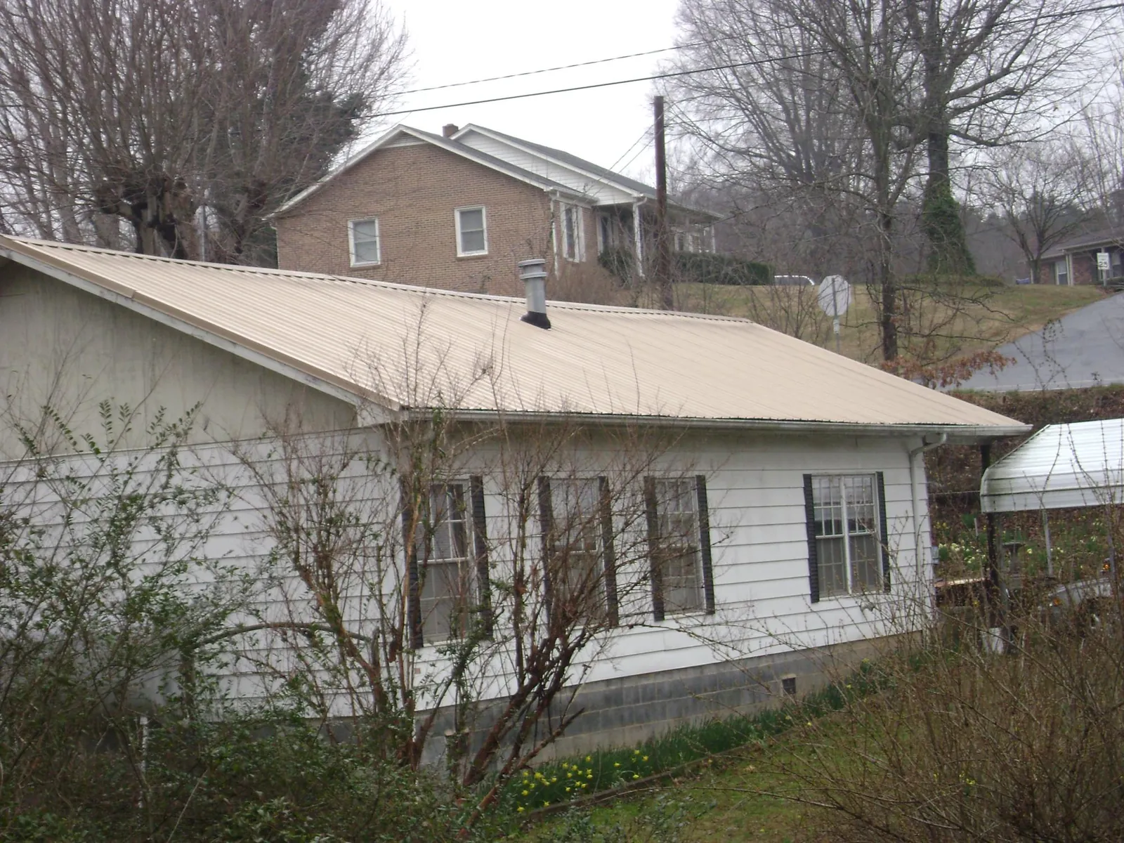 Tan metal roof on a white sided house set into a hillside — Commercial Roofing by Roofing Brothers in New Hampton