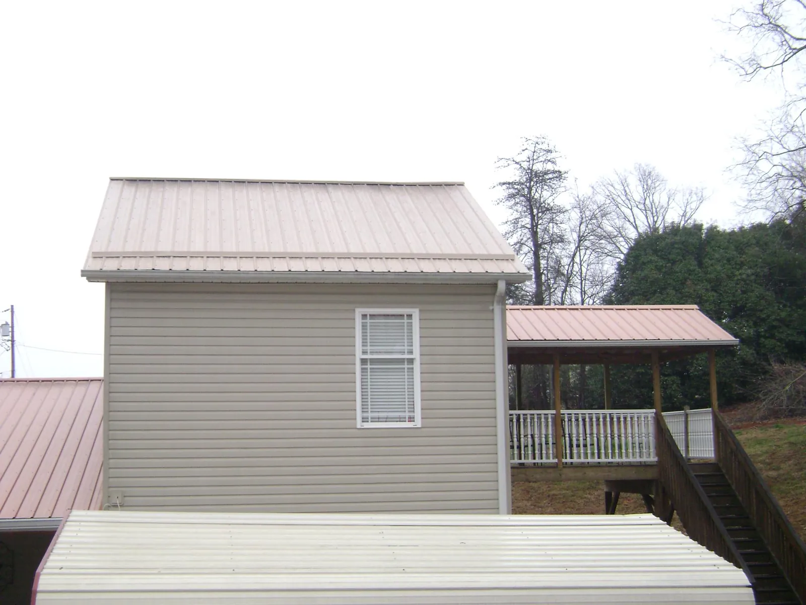 Tan metal roofs on a two story addition and attached porch, from a Roof Replacement job in New Hampton
